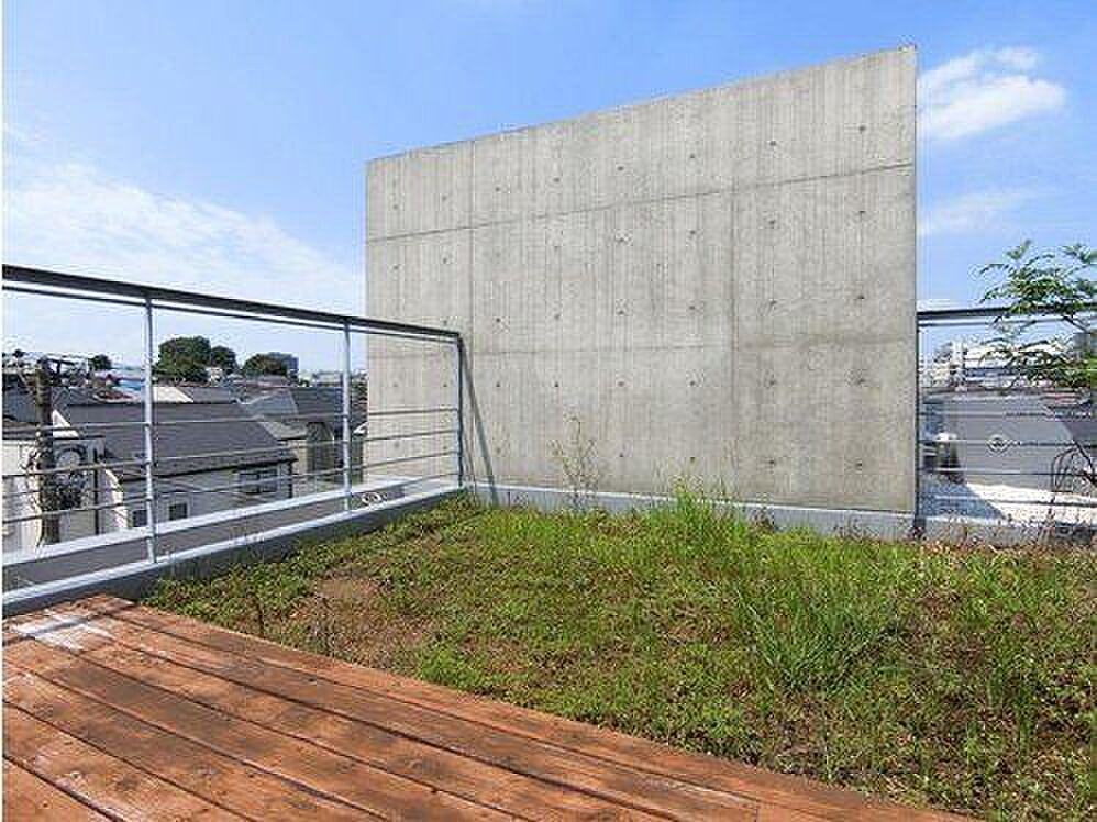 打ち放しの壁を背に、木デッキと草地が同居する屋上